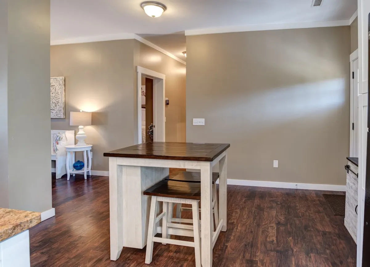 An open-plan dining area with a kitchen island, stools, a modern lamp, and wall art, all set in a warm, inviting atmosphere. The scene hints at family or friends sharing stories and meals, with plenty of space for gatherings and celebrations.