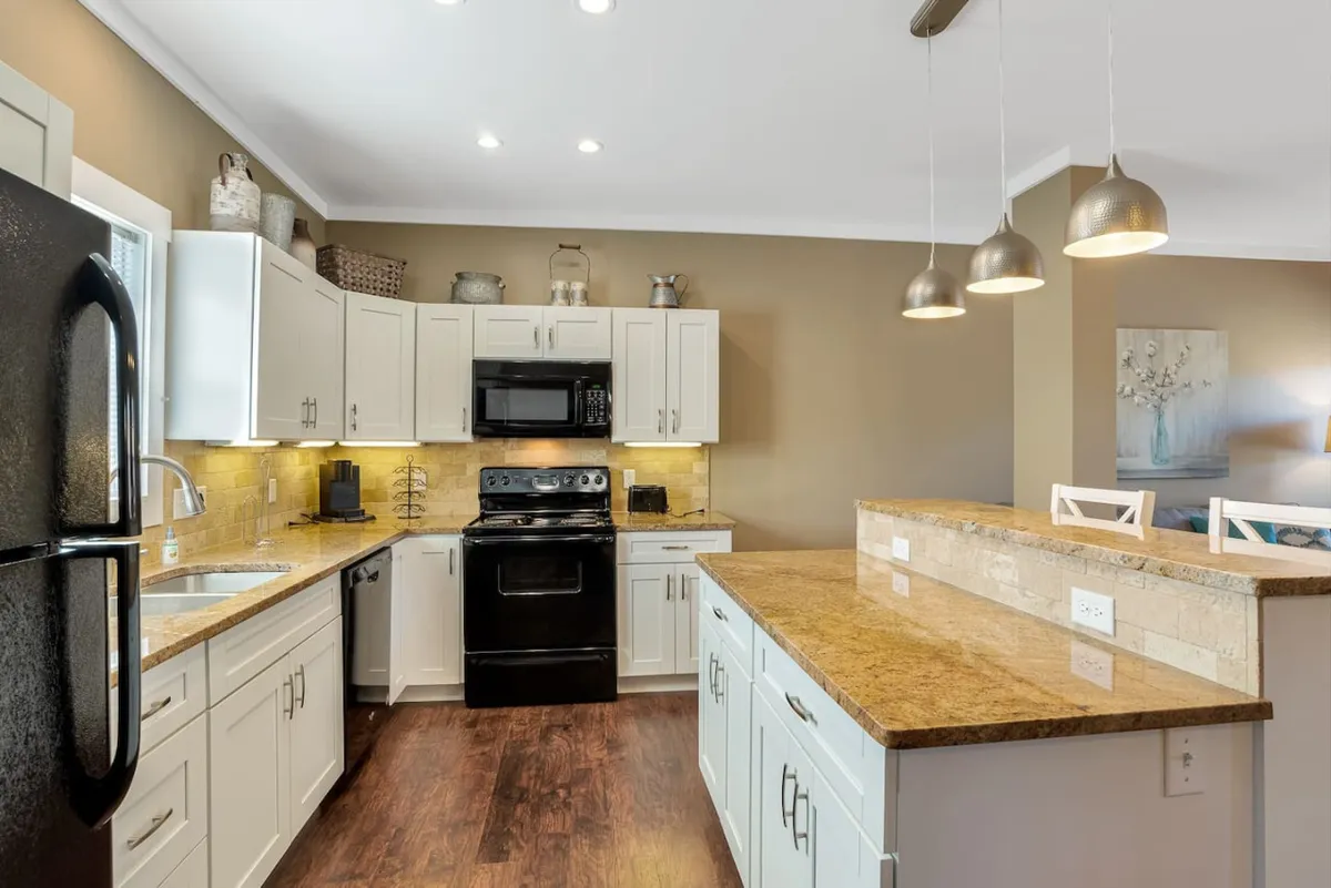 A warm, inviting kitchen featuring a large island, sleek black appliances, granite countertops, and stylish pendant lighting. The setup is ideal for cooking, gathering, and enjoying meals together, with enough space for multiple people to participate. The scene evokes the spirit of hosting, from baking cookies with family to savoring coffee in the morning.