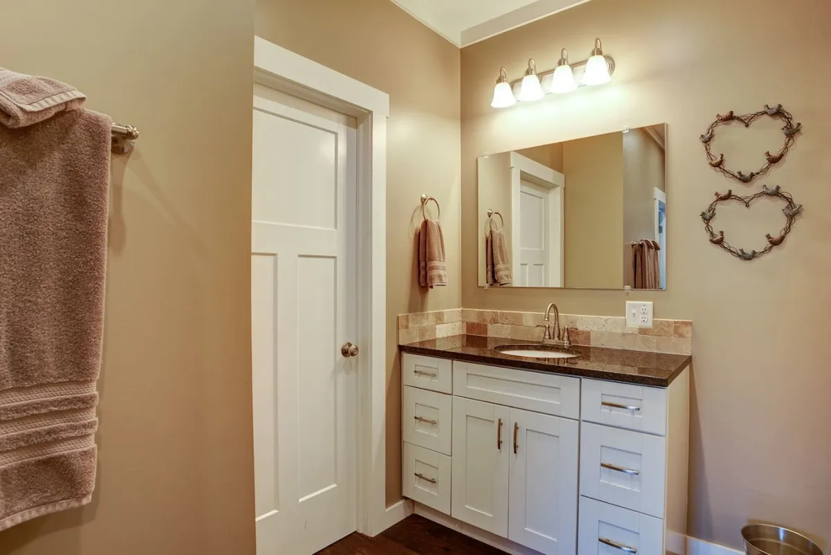 An inviting bathroom vignette with a well-lit vanity, mirror, and neatly arranged towel rack. The scene captures a cozy mood ideal for self-care routines or sharing light-hearted moments. The space is both functional and soothing, designed for morning refreshment or unwinding after a day out.