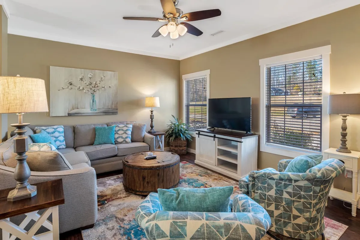 A spacious living room featuring a comfortable sofa, armchairs, coffee table, TV, and a softly glowing lamp. The arrangement encourages both relaxation and social interaction, aligning perfectly with the idea of gathering for slow mornings or lively evenings.