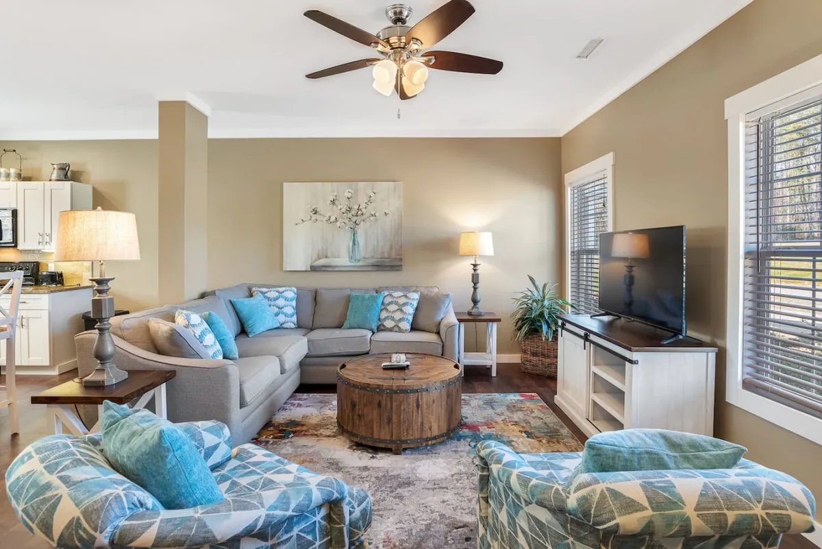 A welcoming living area featuring a plush sofa, coffee table, television, tasteful artwork, and soft lighting from lamps. The space is designed for comfort and socializing, ideal for both relaxing evenings and lively gatherings. Decor elements and layout emphasize a homey yet refined ambiance.
